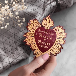 K&ouml;nnte beinhalten: Save the Date Karte mit einem roten Herzen und goldenen Flammen. Der Text lautet "Save the Date Renata & Gerald 06.08.2024".