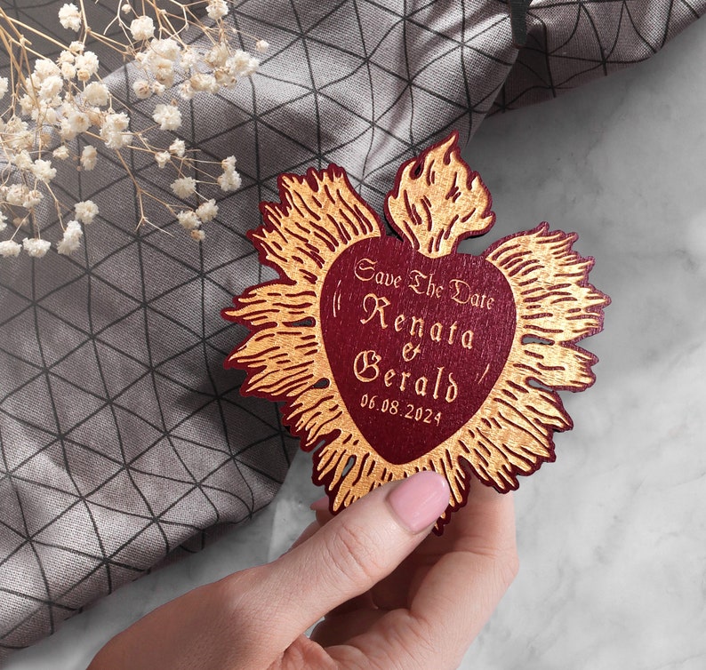 K&ouml;nnte beinhalten: Save the Date Karte mit einem roten Herzen und goldenen Flammen. Der Text lautet "Save the Date Renata & Gerald 06.08.2024".