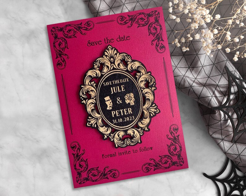 Puede incluir: Una tarjeta roja de guardar la fecha con bordes negros ornamentados y un marco dorado ornamentado con el texto "Save the Date Jule & Peter 31.10.2023" en su interior. El texto "Formal invite to follow" est&aacute; en la parte inferior de la tarjeta.
