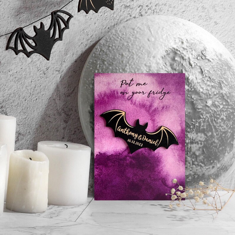 May include: A purple and black bat-shaped wooden magnet with the text "Put me on your fridge" and "Anthony & Daniel 10.13.2023" on it.