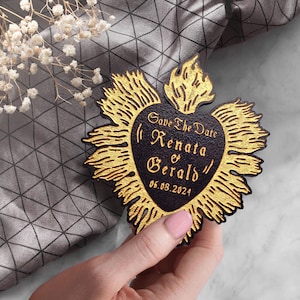 K&ouml;nnte beinhalten: Save the Date Karte in Herzform mit goldenen Flammen darum herum. Der Text auf der Karte lautet "Save the Date Renata & Gerald 06.08.2024"