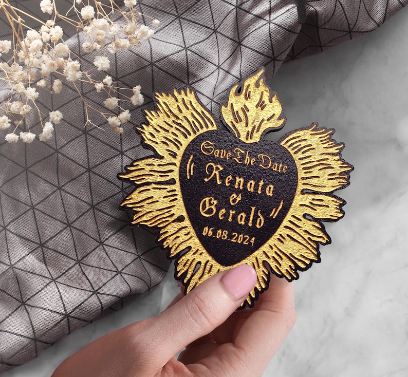 K&ouml;nnte beinhalten: Save the Date Karte in Herzform mit goldenen Flammen darum herum. Der Text auf der Karte lautet "Save the Date Renata & Gerald 06.08.2024"