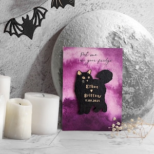 May include: A black cat-shaped magnet with the names "Ethan" and "Brittany" and the date "11.09.2024" on a purple watercolor background. The text "Put me on your fridge" is written at the top. Decorative candles and bat cutouts are in the background.