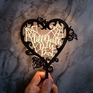 Könnte beinhalten: Schwarzer Herz-förmiger Kuchentopper aus Metall mit Spinnennetz-Design und dem Text "Till Death Do Us Part".