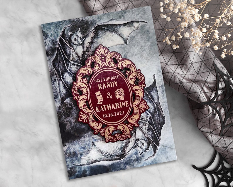 Puede incluir: Tarjeta de guardar la fecha con un marco adornado en color burdeos y dorado con el texto "Save the Date Randy & Katharine 10.26.2023" y una ilustraci&oacute;n en blanco y negro de murci&eacute;lagos.