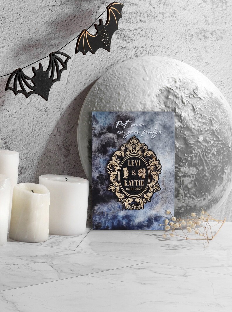 Puede incluir: Una tarjeta de anuncio de boda azul y negra con un marco dorado adornado. El texto dice "Put me on your fridge" y "Levi & Kaytie 04.01.2023".