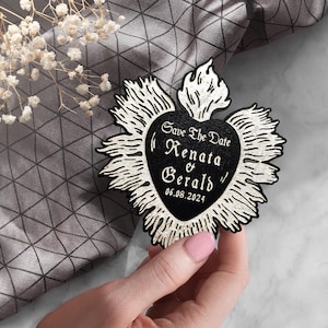 K&ouml;nnte beinhalten: Schwarz-wei&szlig;e Save-the-Date-Karte in Herzform mit einer Flamme oben. Der Text lautet "Save the Date Renata & Gerald 06.08.2024"