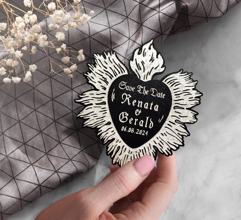 K&ouml;nnte beinhalten: Schwarz-wei&szlig;e Save-the-Date-Karte in Herzform mit einer Flamme oben. Der Text lautet "Save the Date Renata & Gerald 06.08.2024"
