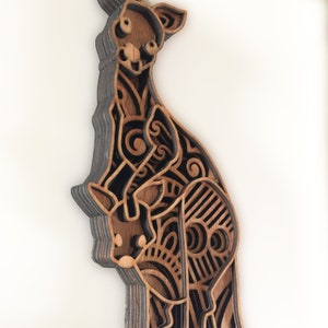 May include: A wooden cutout of a kangaroo with a joey in its pouch. The kangaroo is intricately designed with a layered, patterned design in shades of brown and black.