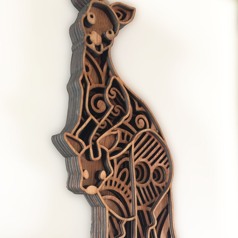 May include: A wooden cutout of a kangaroo with a joey in its pouch. The kangaroo is intricately designed with a layered, patterned design in shades of brown and black.