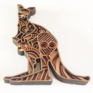 May include: A wooden layered art piece of a kangaroo with a joey in its pouch. The kangaroo is intricately carved with a geometric pattern and is made of multiple layers of wood.