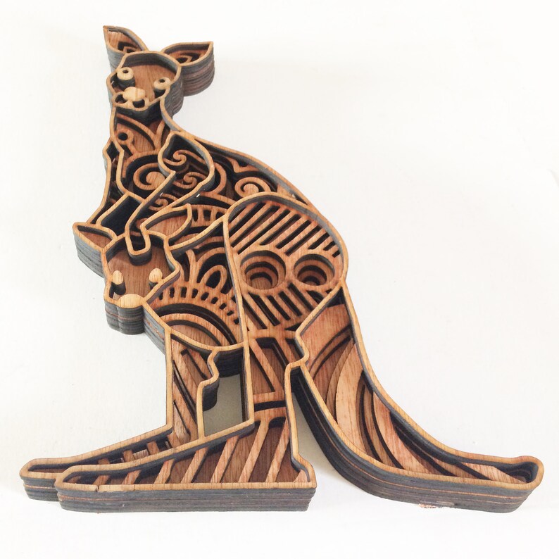 May include: A wooden layered art piece of a kangaroo with a joey in its pouch. The kangaroo is intricately carved with a geometric pattern and is made of multiple layers of wood.