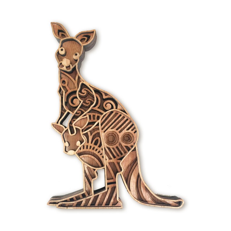 May include: A wooden cutout of a kangaroo with a joey in its pouch. The kangaroo is intricately carved with a geometric pattern in shades of brown.
