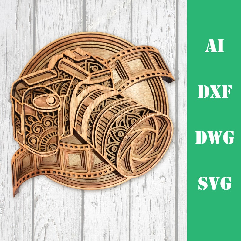 Pode incluir: Uma pe&ccedil;a de arte em madeira em camadas que retrata uma c&acirc;mera com uma tira de filme, mostrando padr&otilde;es e designs intrincados. A obra de arte &eacute; em tons de marrom e bege, com o texto "AI, DXF, DWG, SVG" em branco sobre um fundo verde.