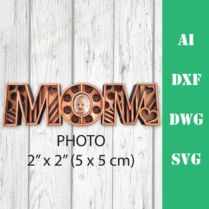May include: Wooden cutout of the word "MOM" with a photo frame in the "O". The frame is 2 inches by 2 inches (5 cm by 5 cm).