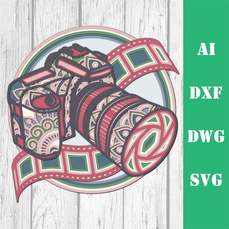Pode incluir: Um design de arte em papel em camadas de uma c&acirc;mera com uma lente, uma tira de filme e um fundo circular. A c&acirc;mera e a tira de filme s&atilde;o em tons de rosa, verde e cinza. O texto "AI, DXF, DWG, SVG" est&aacute; &agrave; direita.