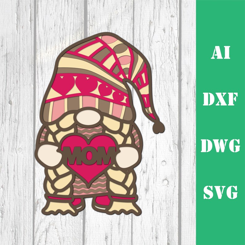 May include: A layered papercraft gnome holding a red heart with the word "MOM" on it. The gnome has a brown hat with pink and brown stripes and a white beard. The gnome is standing on a white wooden background.