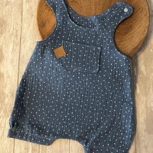 May include: Blue romper with white polka dots. The sleeveless garment has a front pocket and a small brown leather patch. The romper has snap closures on the straps. The garment is made of a textured fabric.