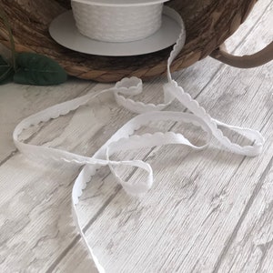 May include: White elastic trim with a scalloped edge. The trim is rolled up on a spool.
