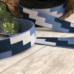 Könnte beinhalten: Eine Rolle blau-weiß gemustertes Band. Das Band zeigt ein sich wiederholendes geometrisches Design in Blau- und Weißtönen. Das Band besteht aus einem gewebten Material und eignet sich für Bastelarbeiten und dekorative Zwecke.