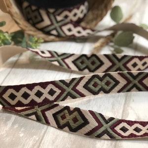 May include: Decorative ribbon with a geometric pattern in burgundy, olive green, and cream. The ribbon is displayed in a roll and in a length, showcasing the repeating design. The ribbon is likely used for crafts or embellishments.