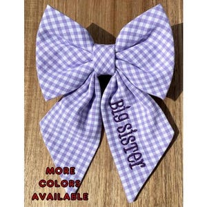 May include: A purple and white gingham bow tie with the text "Big Sister" embroidered in purple.