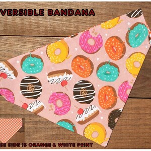 May include: Reversible bandana with a pink background and a donut print. The reverse side is orange and white.
