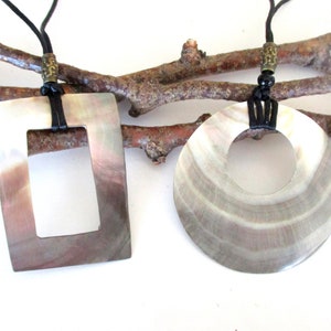 May include: Two shell necklaces with black leather cords. One necklace features a rectangular shell pendant with a cutout in the center. The other necklace features a round shell pendant with a hole in the center.