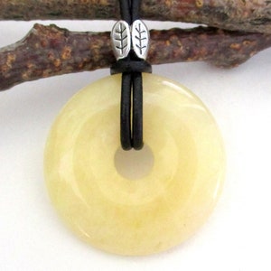 May include: A yellow jade donut pendant on a black leather cord with silver leaf accents.