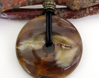 May include: A round, polished pendant necklace with a brown and tan marbled pattern. The pendant is suspended from a black leather cord with a decorative bronze-colored bead. The necklace is a natural stone jewelry.