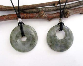 May include: Two circular green stone pendants with a mottled texture, each suspended on a black cord. The left pendant features a smooth silver bead, while the right pendant includes a textured silver spacer bead above the stone ring.