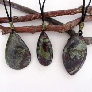 May include: Three teardrop-shaped pendants with a green, black, and red marbled pattern, hanging from black cords with gold-toned clasps.