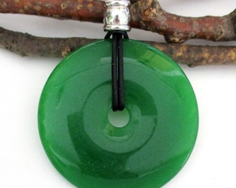 May include: A circular green stone pendant with a smooth, polished finish and a central hole. The pendant is suspended from a black cord that passes through a silver-toned metal bead, securing the stone in place for wear as a necklace.