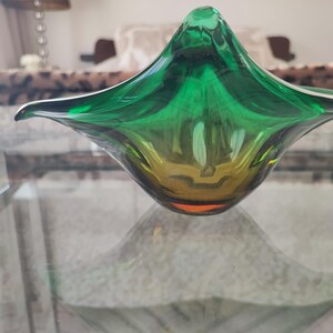 May include: A decorative glass bowl with a unique, organic shape. The bowl transitions from a deep green at the top to a golden yellow at the base. Its form is reminiscent of a flower or a stylized leaf, adding a touch of elegance to any space.