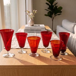 Puede incluir: Un conjunto de seis copas de cristal rojo vibrante con tallos y bases circulares transparentes. Las copas varían ligeramente en altura y forma, presentando un acabado liso y translúcido que capta la luz de manera uniforme.