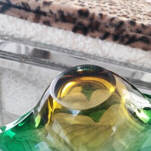 May include: A decorative glass bowl with a unique shape and color gradient. The bowl transitions from a vibrant green at the edges to a golden yellow in the center. The bowl is on a glass surface.
