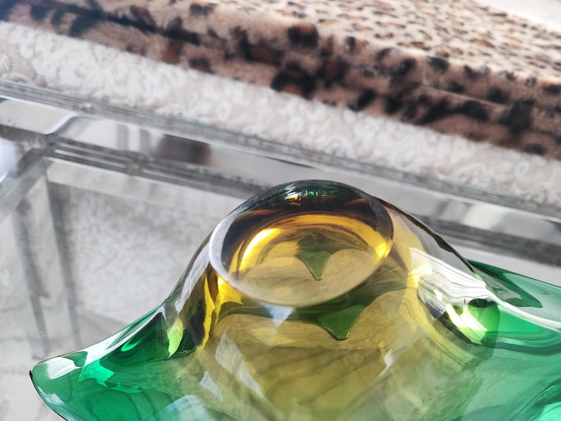 May include: A decorative glass bowl with a unique shape and color gradient. The bowl transitions from a vibrant green at the edges to a golden yellow in the center. The bowl is on a glass surface.