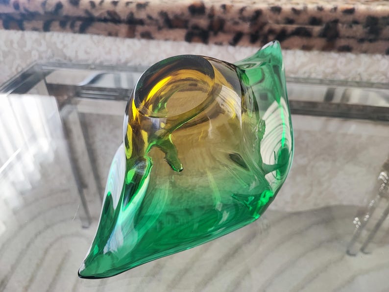May include: A decorative glass bowl with a unique, organic shape. The bowl transitions from a vibrant green at the base to a golden-yellow hue at the top. Its smooth, curved design adds a touch of elegance to any space.