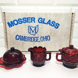 Può includere: Un set di tre piatti da portata in vetro rosso rubino. Il set comprende una burriera coperta, una lattiera e una zuccheriera coperta. La scatola dietro i piatti recita "MOSSER GLASS CAMBRIDGE, OHIO."