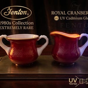 May include: A Fenton Royal Cranberry glass sugar bowl and creamer set from the 1980s collection. The pieces feature a deep red body with white handles and gold rim detailing. Text on the image reads Fenton, 1980s Collection, EXTREMELY RARE, ROYAL CRANBERRY, UV Cadmium Glow, FENTON ART GLASS, and UV TESTED.