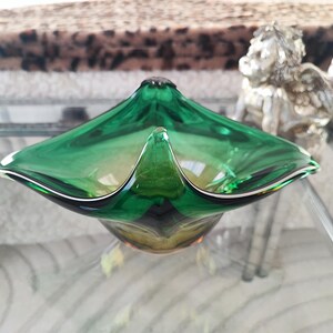 May include: A vibrant green glass bowl with a unique, flared design. The bowl has a glossy finish and a distinctive shape, perfect for decorative use. The bowl is approximately 10 inches wide.