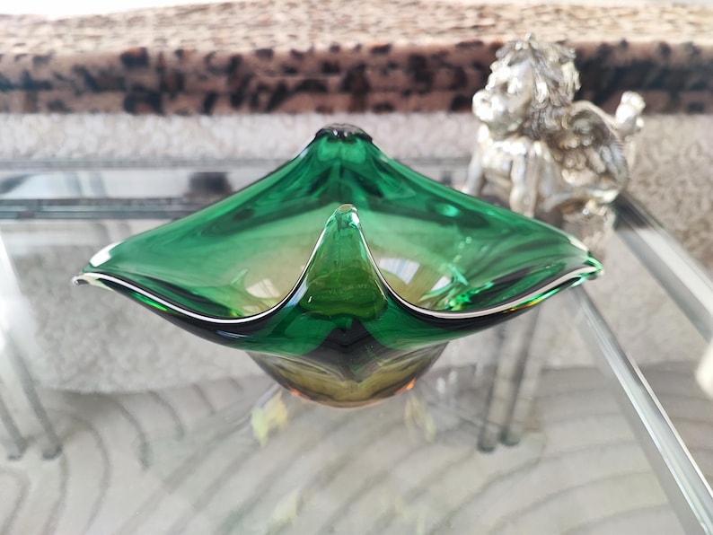 May include: A vibrant green glass bowl with a unique, flared design. The bowl has a glossy finish and a distinctive shape, perfect for decorative use. The bowl is approximately 10 inches wide.