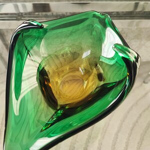 May include: A handcrafted glass bowl with a unique shape, featuring a vibrant green exterior and a golden-yellow interior. The bowl's design is organic and flowing, with a glossy finish. This decorative piece is ideal for home decor.