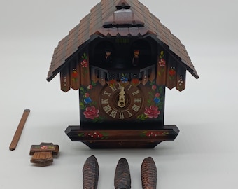 Könnte beinhalten: Eine traditionelle Holzkuckucksuhr mit brauner Lackierung und aufwendigen Details. Das Zifferblatt der Uhr zeigt römische Ziffern und ein handgemaltes Blumenmuster. Die Uhr ist in Deutschland hergestellt und hat ein Pendel und einen Kuckucksvogel.