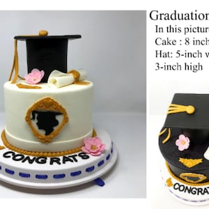 Puede incluir: Un pastel de graduaci&oacute;n con birrete negro, diploma y decoraciones de flores rosas. El pastel blanco tiene un marco dorado y una silueta de graduado. El pastel mide 20 cm de di&aacute;metro y tiene la palabra "CONGRATS" en la base.