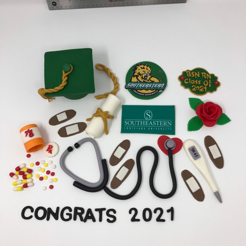 Puede incluir: Un conjunto de decoraciones de graduaci&oacute;n, que incluyen un birrete verde, un diploma y elementos m&eacute;dicos como un estetoscopio, un term&oacute;metro y vendas. El texto "CONGRATS 2021" se muestra en la parte inferior, con logotipos universitarios y una rosa.