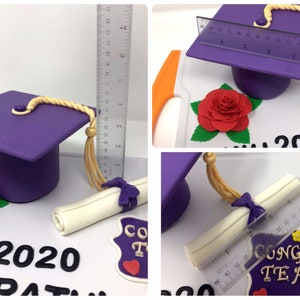 Puede incluir: Decoraci&oacute;n de pastel con tem&aacute;tica de graduaci&oacute;n que presenta un birrete morado con borla dorada, un diploma enrollado atado con una cinta morada y una rosa roja. El pastel est&aacute; decorado con el texto "2020" y "Felicidades Teagan".