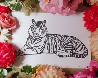 May include: A black and white line art print of a tiger lying down. The print is on white paper and has the artist's signature in the bottom right corner.