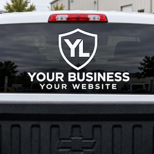 May include: A white vinyl decal applied to the rear window of a pickup truck. The design features a shield icon with the letters YL inside, followed by the text YOUR BUSINESS and YOUR WEBSITE in a clean, bold, sans-serif white font.