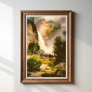 May include: A framed landscape print featuring a waterfall cascading down a rocky cliff. The artwork showcases a vibrant scene with lush greenery, trees, and boulders, all bathed in soft, natural light. The frame is made of wood.